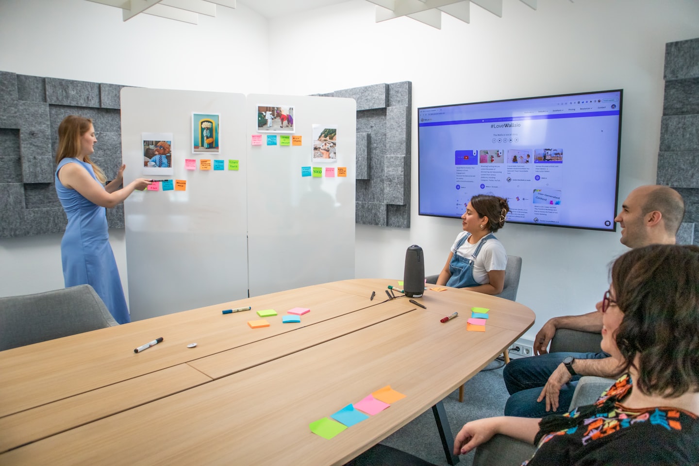 Donna in abito blu aggiunge post-it a una lavagna durante una riunione di squadra.