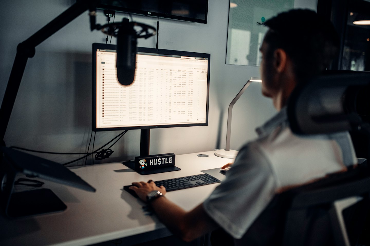 Persona che lavora al computer su una scrivania d'ufficio con un cartello 'HUSTLE'.
